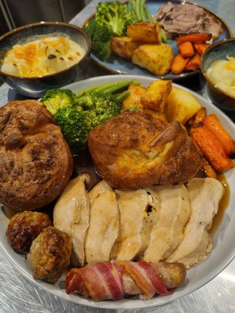 A large Sunday roast with sliced meat, two Yorkshire puddings, pig in blanket, stuffing, broccoli, green beans and carrots