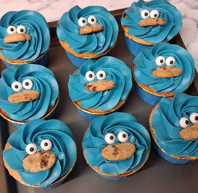 Blue-iced cupcakes decorated as Cookie Monster with sugar eyes and a mini cookie