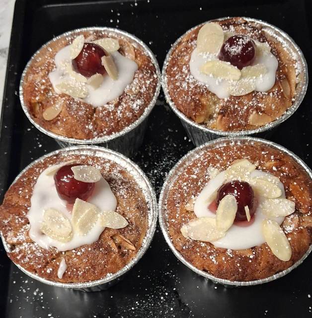 Four almond and cherry cakes topped with icing, flaked almonds and a glacé cherry